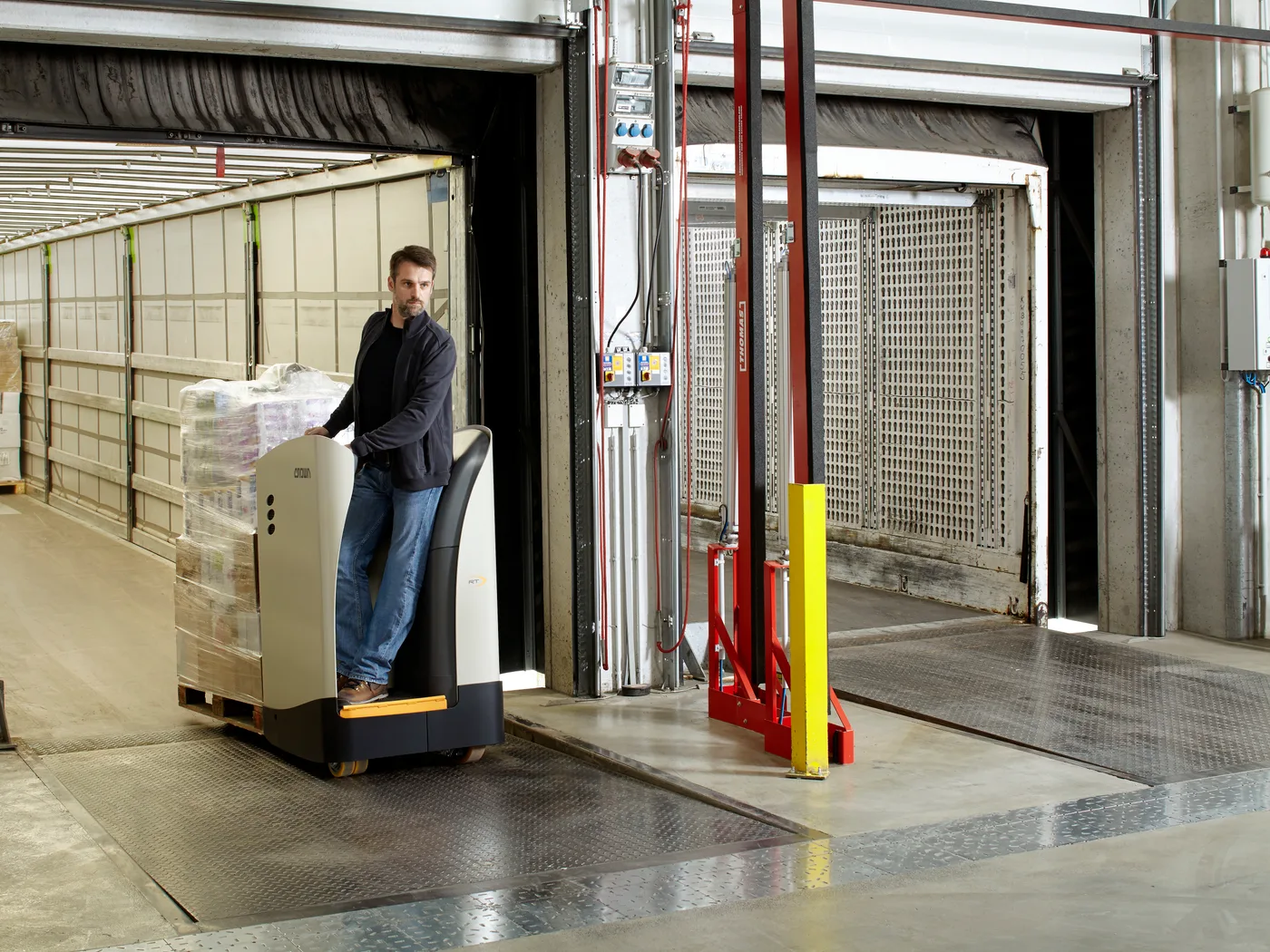 Operator on a Crown rider pallet truck unloading a trailer at a dock door