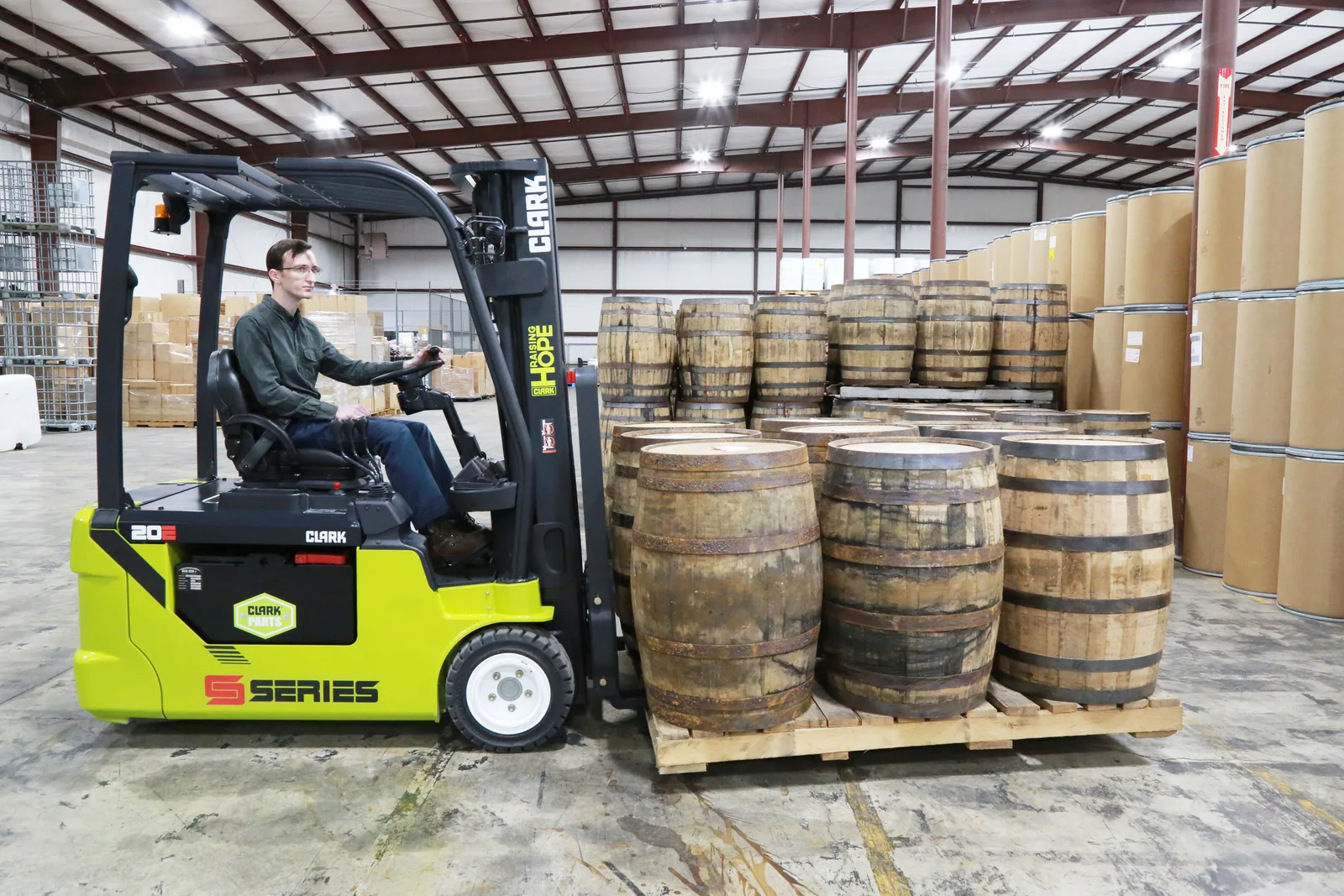 Clark electric forklift moving a pallet of barrels in a warehouse